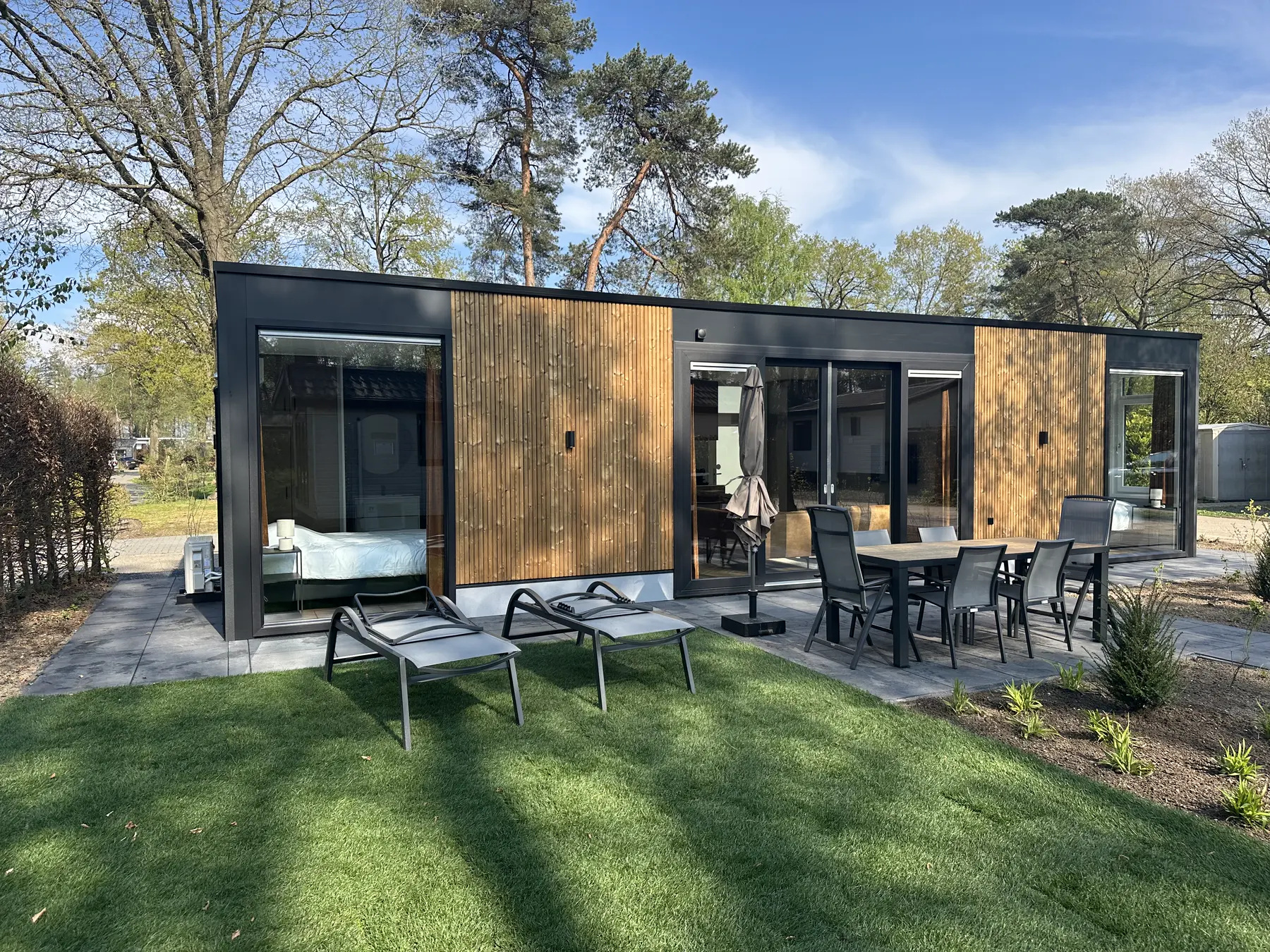De lodge vanuit de zonnige tuin, met terras en ligbedden op het gras